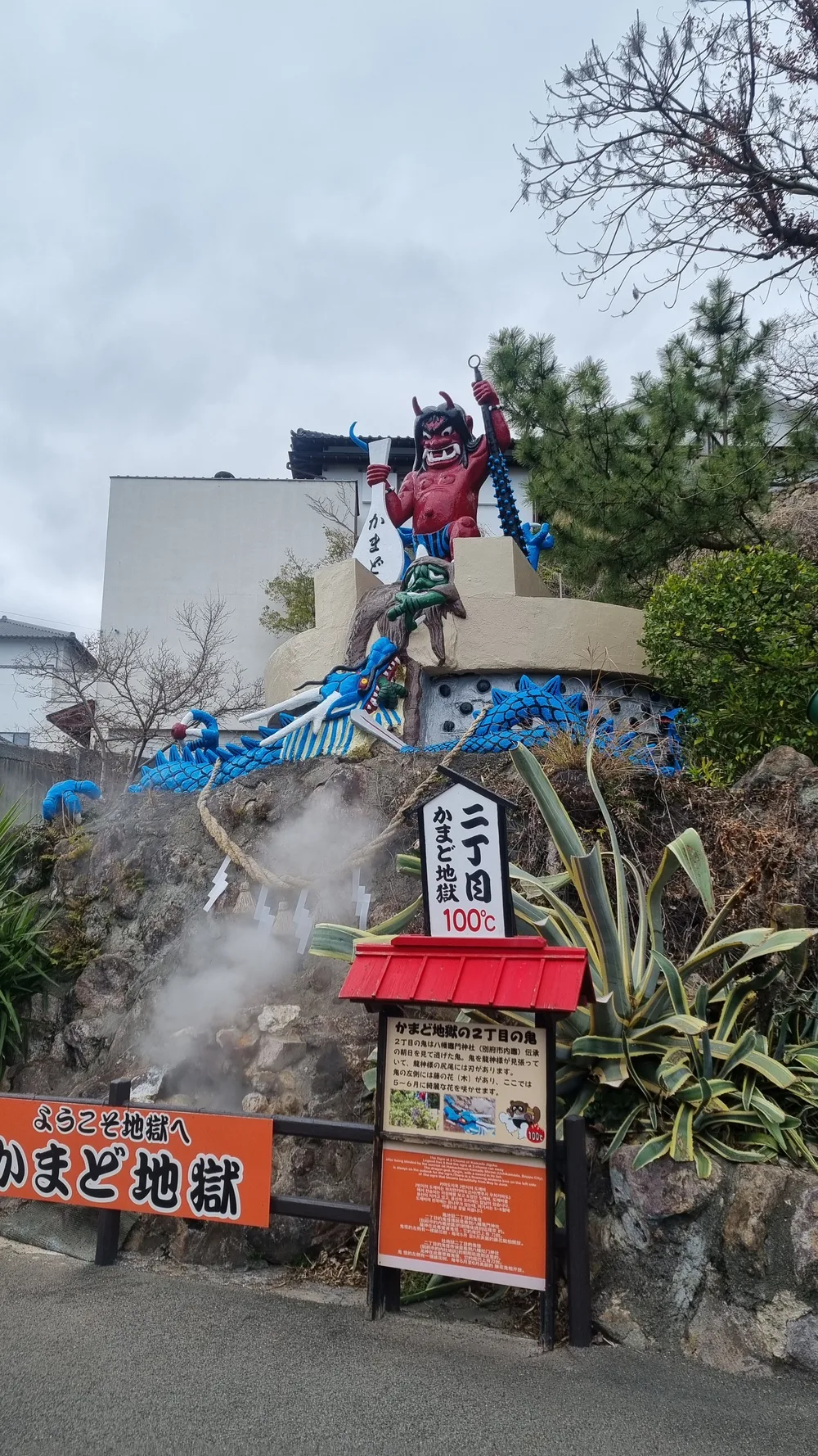 The red demon statue at the entrance to Kamado Jigoku, with steam rising behind the signboard